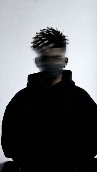 A stylized, blurry photo of a person wearing a black hoodie, with their face obscured by a digital glitch effect.