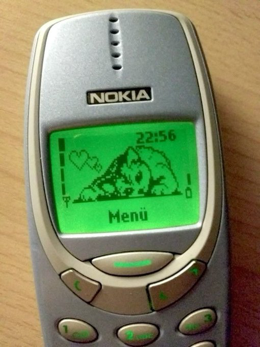 A Nokia mobile phone displays a green screen with a cat illustration, the time 22:56, and the word 'Menü' in the center.