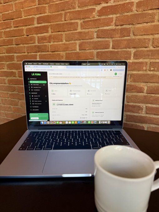 A MacBook on a desk displaying the 'LA FORA' platform in Spanish, with a white mug beside it against a brick wall background.