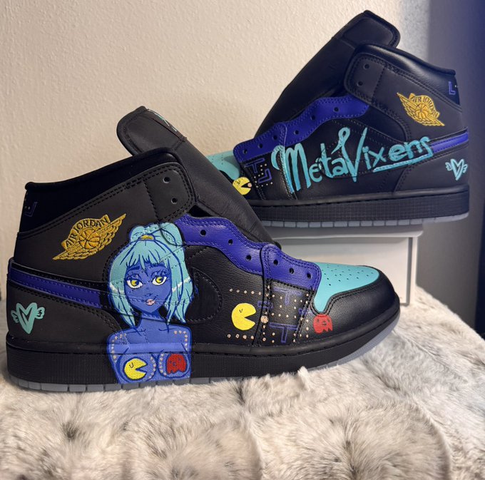 A pair of black, blue, and teal Air Jordan 1 sneakers custom-painted with 'MetaVixens' text, Pac-Man imagery, and an anime-style blue-haired girl character.