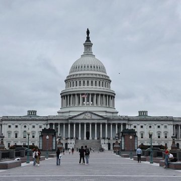 The U.S. Capitol building stands under a cloudy sky, with visitors gathered in the plaza below, as President Trump has stated he would accept placing his cryptocurrency holdings in a blind trust under the CLARITY Act.