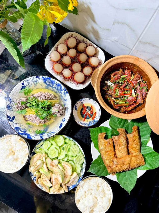 A family-style spread of Vietnamese dishes—including steamed rice, braised pork with eggs, beef in broth, a clay pot stir-fry, fried fish on betel leaves, and fresh vegetables—is arranged on a dark countertop, perfectly capturing the post's invitation to pause the busy day and gather for a simple, comforting meal together.