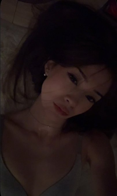 A young woman with long dark hair lies down looking at the camera in a dimly lit selfie, wearing a tank top and small earrings. The moody, intimate photo accompanies the caption "max win," suggesting a celebratory or triumphant personal moment being shared.