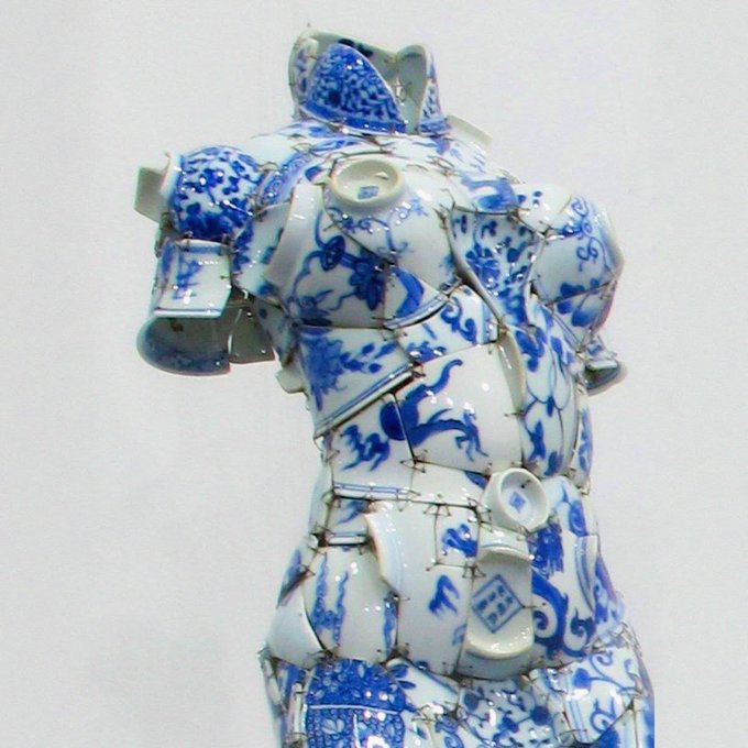 A sculpture of a torso constructed from fragmented blue and white porcelain pieces reassembled and bound together with visible wire.