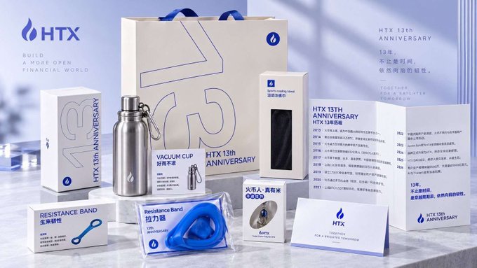 A promotional display for HTX's 13th Anniversary featuring branded merchandise including a vacuum cup, resistance bands, a stainless steel water bottle, a spotlight lamp, and various boxes with the HTX logo.