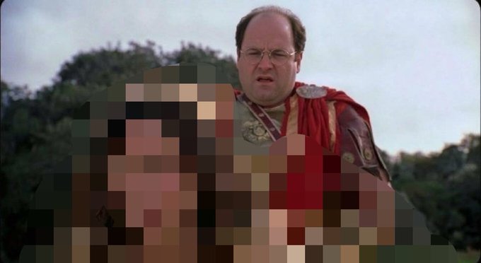 The character George Costanza from Seinfeld, dressed in a red toga-like costume with a medallion, looks confused at a heavily pixelated object or person in the foreground.