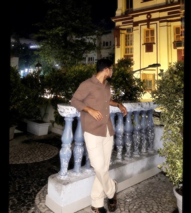 A young man in a brown shirt and cream pants poses confidently against an ornate blue-and-white balustrade at night, with a brightly lit classical building in the background. The image suggests a personal moment shared alongside a post expressing support for Portugal, likely to give a human face to his betting positions on Polymarket.