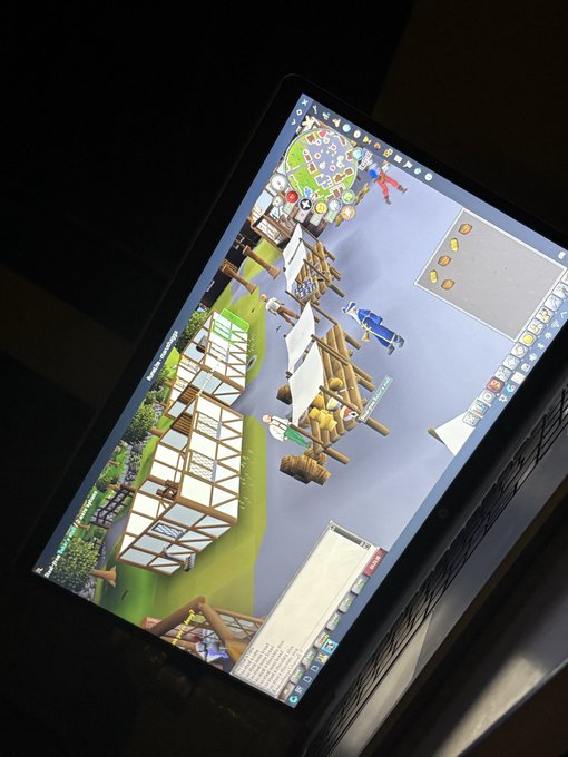 A laptop screen displaying an isometric 3D simulation or game featuring medieval-style buildings, windmills, and characters in a village setting.