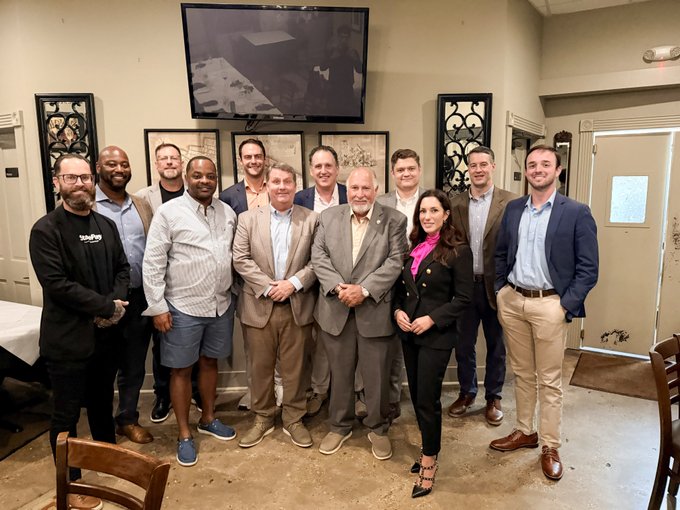 A diverse group of professionals pose for a group photo at an indoor dinner venue, with a "YouTube" branded jacket visible on one attendee. The image captures attendees of The Digital Chamber State Network and Chainlink leadership dinner held ahead of the StateChain Summit 2026, gathering key figures for networking and discussions about blockchain's future role in state-level policy and innovation.