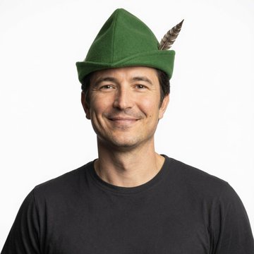 A man wearing a black t-shirt and a green Robin Hood-style hat with a feather, smiling against a plain white background.