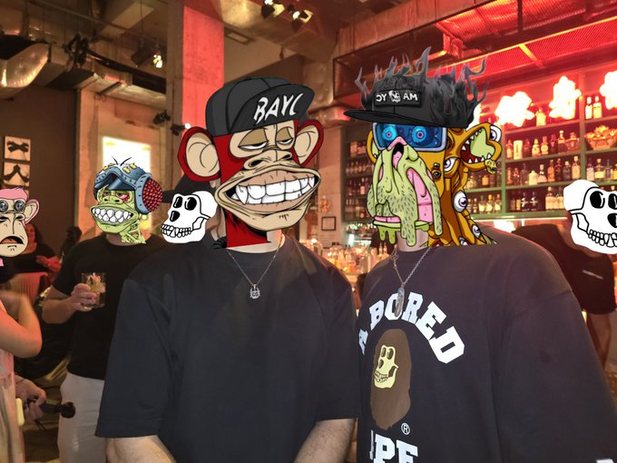 Two people pose at a bar in Hong Kong wearing Bored Ape Yacht Club NFT profile filters—one sporting an ape in a "BAYC" cap and the other wearing a mutant ape with a "YGY SLAM" cap—while the person on the right also wears a "BORED APE" t-shirt, capturing the Yuga Asia Tour Hong Kong community gathering.