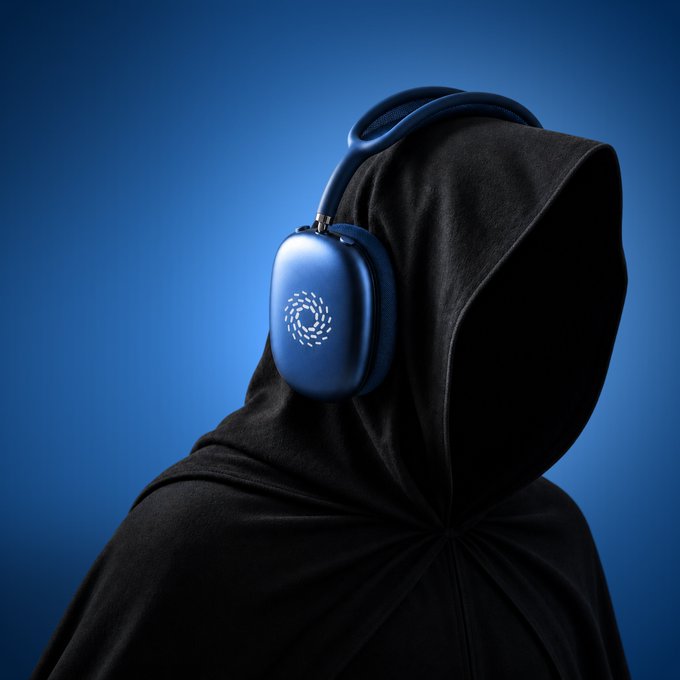 A product photo of blue Dyson on-ear headphones with a glowing circular logo, worn by a person in a black hooded garment against a blue background.
