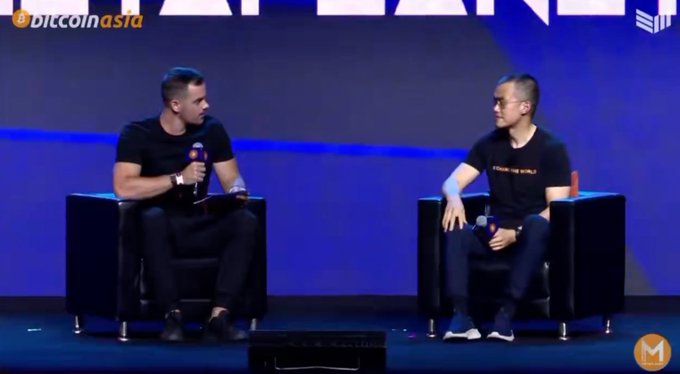 Two men sitting in black chairs on a stage at a 'Bitcoin Asia' event, with one holding a microphone.