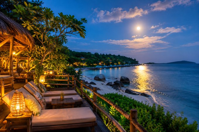 A tranquil twilight beach scene from a resort deck, featuring lounge seating, glowing lanterns, and the moon reflecting on calm ocean waters.