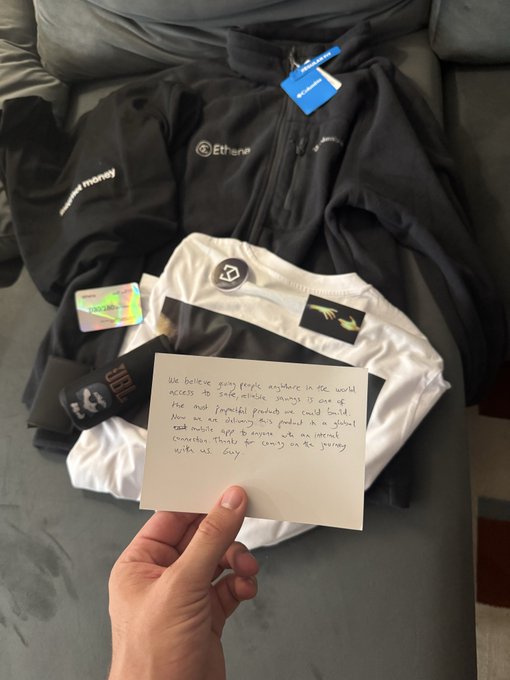 A hand holds a handwritten note over cycling gear (jackets with 'goat money' and 'Etienne' logos) that reads about gifting the products to friends in critical care and providing a small mobility app to anyone in an internal evacuation, thanking buyers for helping people in Gaza.