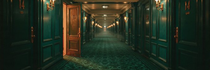 A long, dimly lit corridor with green-paneled walls, vintage wall sconces, and numbered doors (10 and 14 visible), with warm orange light spilling from an open door on the left.