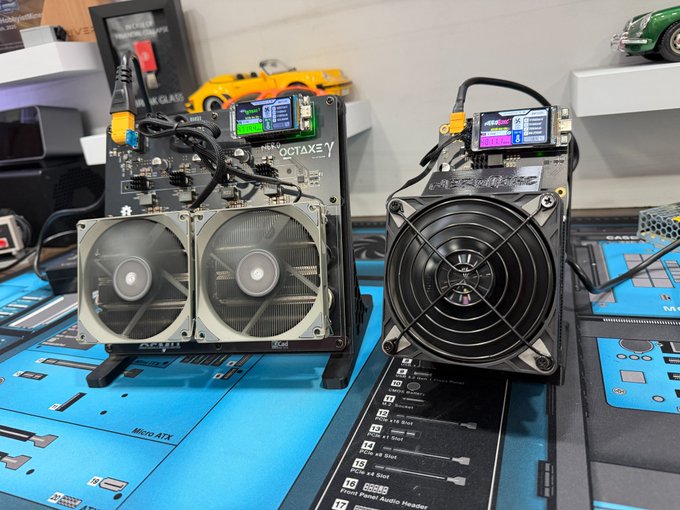 Two DIY electronics projects, possibly custom coolers or fans, with digital displays sit on a blue Micro ATX motherboard schematic mat alongside a yellow toy car and various components.