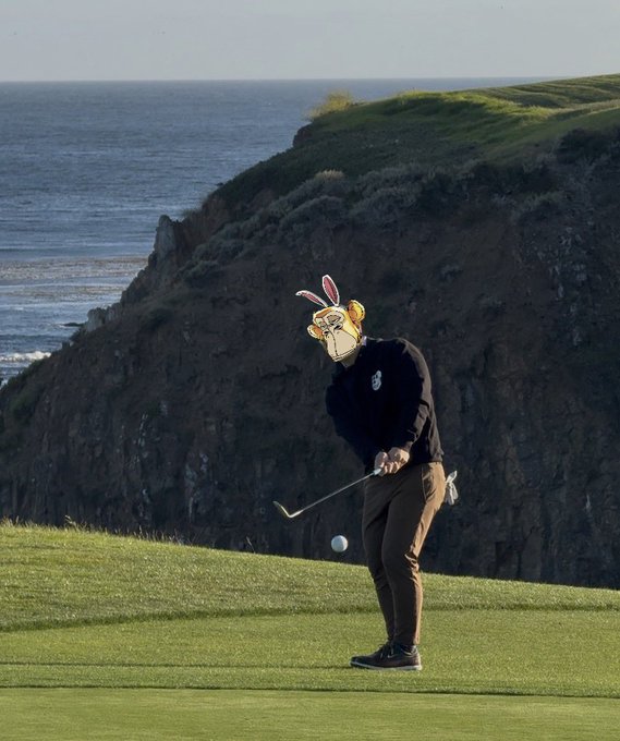 A surreal AI-generated image of a golfer wearing a hoodie, swinging a club on a coastal golf course, but their head is replaced with a bizarre rabbit-like mascot wearing sunglasses.