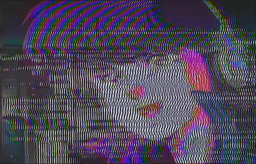 The image shows a distorted, fuzzy picture of a person's face with pink hair. The background appears to be black, but there are stripes of red, blue, green, and purple colors that make up the background. The image also contains text that reads "千卂ᗪ乇 1.6 TEZ".