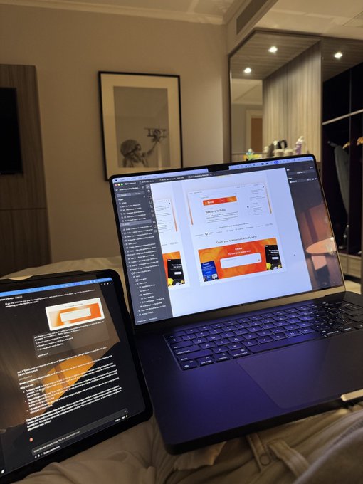 A workspace setup showing a laptop and tablet displaying what appears to be a presentation design interface, sitting on a bed in a hotel-like room.