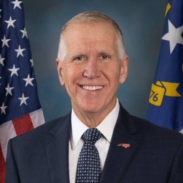 Senator Thom Tillis smiles in an official portrait, standing before an American flag and a North Carolina state flag, as he discusses the White House's engagement on bipartisan Clarity Act ethics legislation.