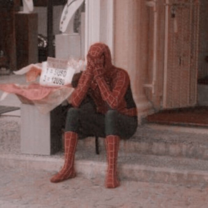 A person dressed in a Spider-Man costume is sitting on some steps with their head in their hands in a dejected posture.