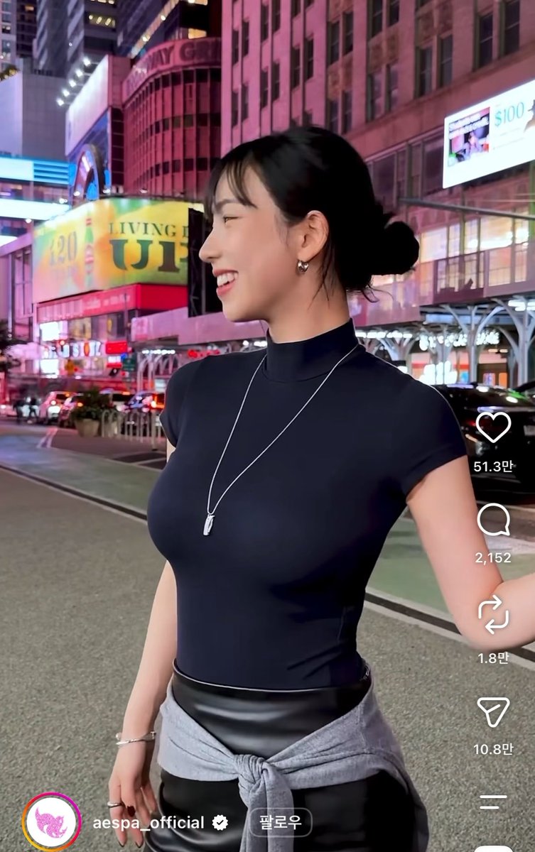 Screenshot of an Instagram post by aespa_official showing a smiling woman in a black top with a necklace, standing on a city street at night, with 51.3만 likes.