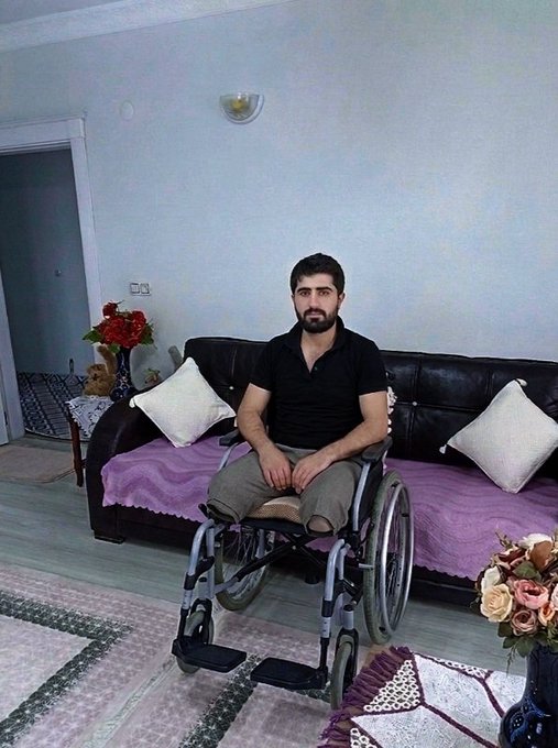 A young man named Can, who survived the devastating February 6 earthquake, sits in a wheelchair in a modest living room, illustrating the lasting physical impact of the disaster on survivors. The image accompanies a heartfelt post seeking to support him through fundraising efforts.
