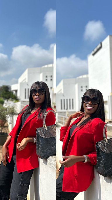 A woman in a bold red blazer and sunglasses poses stylishly outdoors with a designer handbag, the sunny backdrop and fresh energy perfectly capturing the "touched grass" vibe before getting back to the crypto grind.