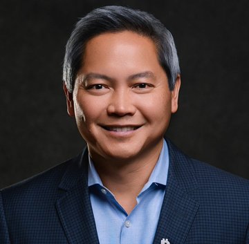 The image features a man wearing a blue shirt with a plaid pattern and a dark suit jacket. He has gray hair and a smile on his face as he looks directly at the camera, giving off an air of confidence and professionalism. The background is black, which contrasts with the man's attire and makes him stand out even more. The image also contains text that reads "Strategy CEO Phong Le doubles down on Bitcoin: We are the largest holder of Bitcoin in the world. The largest buyer of Bitcoin in the world. And we plan to keep it that way." This message emphasizes the importance of Bitcoin as a global currency and highlights Strategy's position as a leader in this emerging technology.