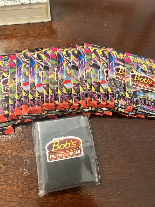 A collection of Pokémon Trading Card Game blister packs featuring Mega Evolution and Pitch Black boosters, along with a 'Bob's Petroleum' deck box containing black sleeves.