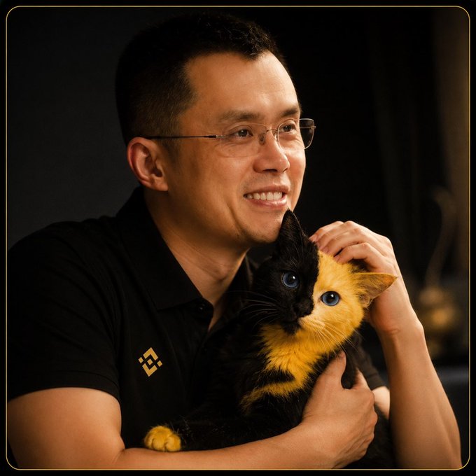 Portrait of a smiling man wearing glasses and a black Binance polo shirt, holding a calico cat.