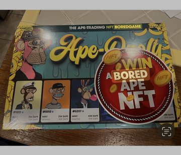 An unopened box of 'Ape-Opoly,' 'The APE-Trading NFT Boredgame,' with a red circular sticker stating 'WIN A BORED APE NFT' placed on top.
