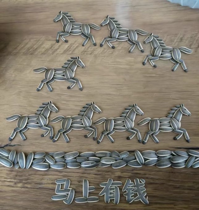 The image features a wooden surface with various horse shapes made from cut-out play dough, arranged in a row. The horses are depicted as running, creating an impression of movement across the scene. In addition to the play dough horses, there is also a line of sunflower seeds placed on the same wooden surface. The arrangement of these elements suggests that they might be part of a creative project or art installation, possibly related to Chinese culture or a celebration involving horses and sunflowers.