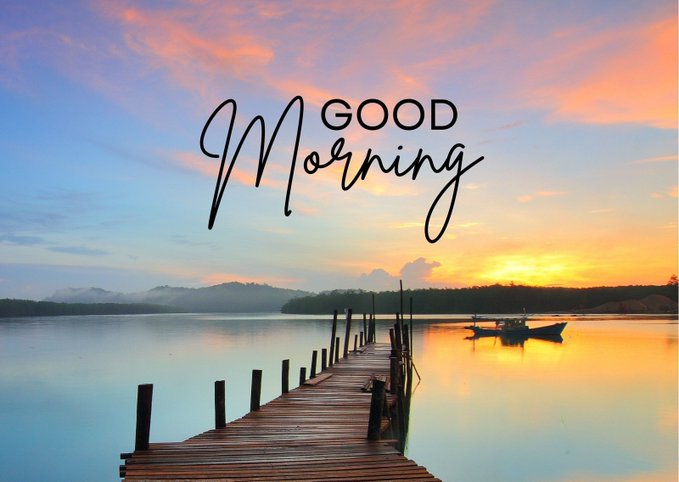 A serene sunrise over a calm lake with a wooden dock extending into the water and a small boat anchored nearby, featuring the text "Good Morning" in elegant script overlaying the colorful sky, fitting the warm morning greeting theme of the post about accumulating River Points and staking $RIVER tokens.