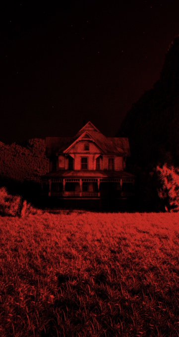 A Victorian-style house stands in a field, illuminated entirely in red against a dark night sky.