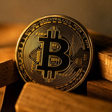 A close-up golden Bitcoin coin featuring the iconic 'B' logo and 'BITCOIN DIGITAL DECENTRALIZED PEER TO PEER' text around its edge.