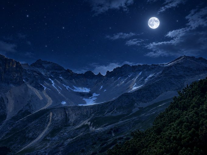 A scenic nighttime mountain landscape illuminated by a full moon and stars.