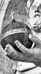 A black and white close-up photograph showing hands cradling a textured coconut-like fruit with a small sprout emerging from the top, while a young child looks on in the background.
