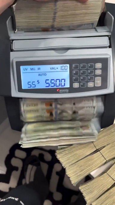 A Cassida currency counter displays a total of 55 bundles totaling $5,600, with stacks of counted cash visible around it—visually reinforcing the "GM = Get Money" hustle message by showing someone actively counting their earnings.