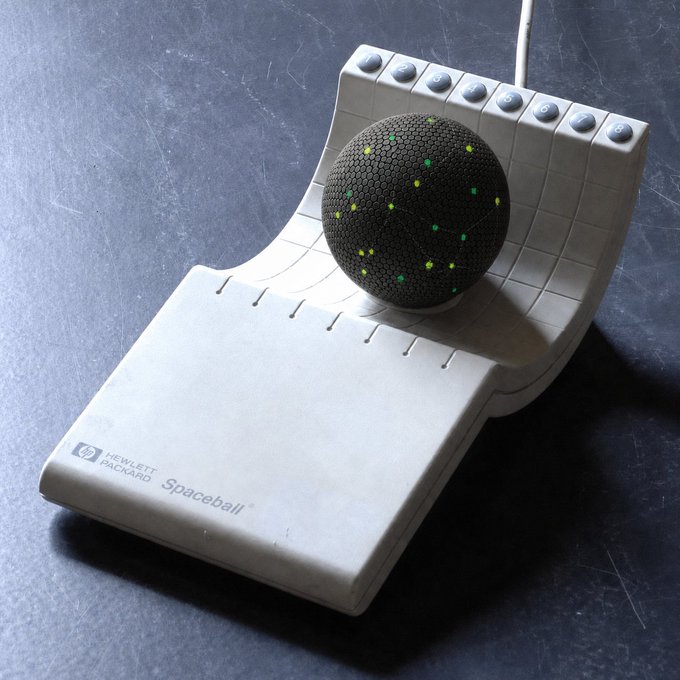 A vintage Hewlett Packard Spaceball, a 3D input device featuring a trackball on a contoured gray base with programmable buttons along the top edge.