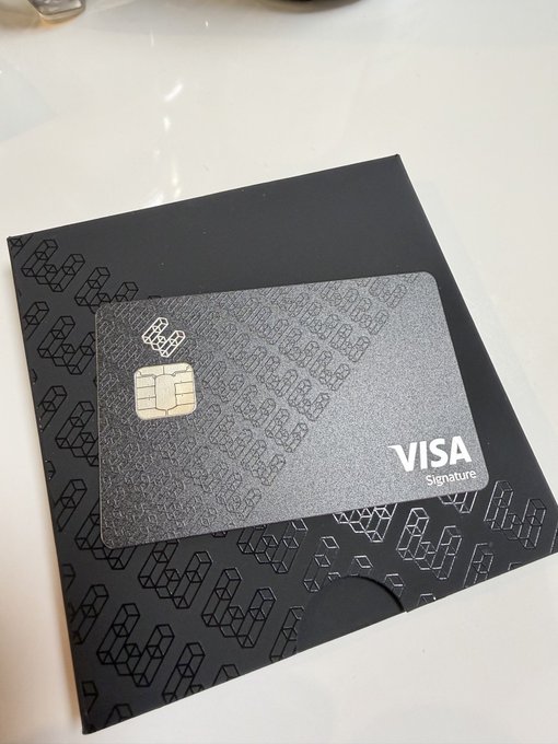 A sleek black metal Visa Signature card with a distinctive geometric pattern rests on a matching dark holder, featuring the "VISA Signature" branding in the bottom right corner and a contactless chip on the front. The image aligns with the post by showcasing the premium aesthetic of the ether.fi (@ether_fi) branded card, emphasizing the refined, luxury design that the post praises.