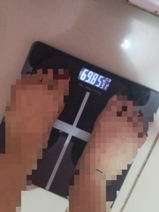 A person stands on a digital scale that displays a weight of 69.85 kg.