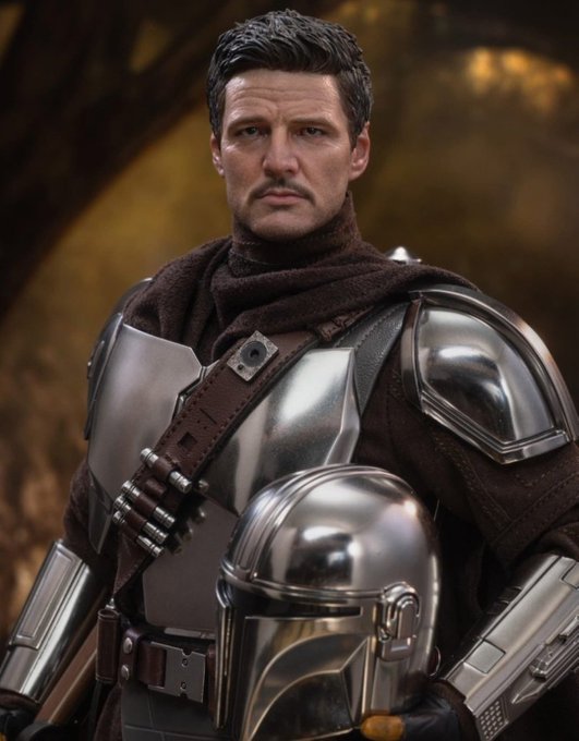 A man dressed in silver Mandalorian-style armor with a brown scarf, holding his helmet, resembling Pedro Pascal.