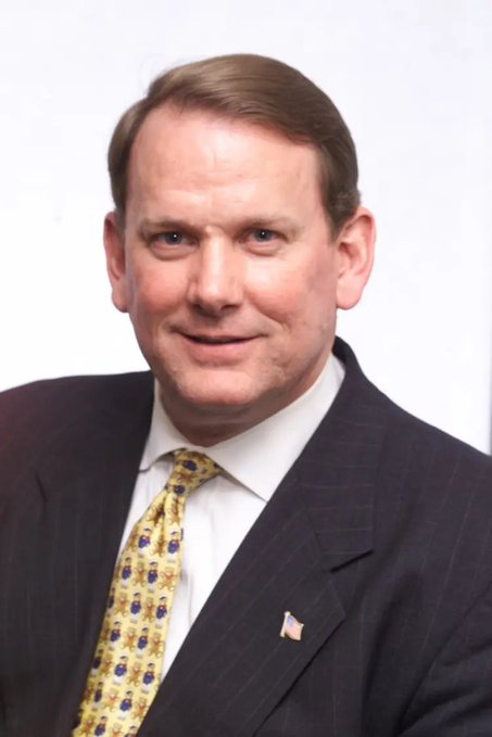 An official portrait of Senator Tom Young of Florida, wearing a dark suit with a yellow patterned tie and an American flag lapel pin.