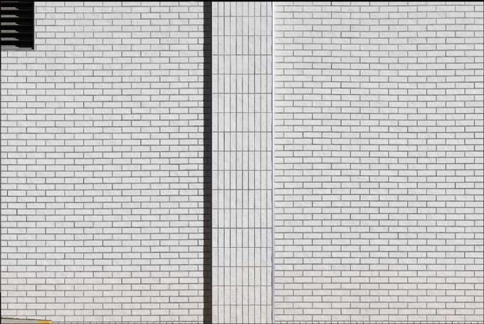 A white brick wall with black vertical dividers and what appears to be a louvered vent in the upper left corner.