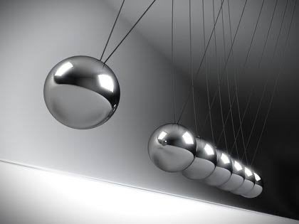 A Newton's cradle with shiny metal spheres, photographed in black and white, showing one sphere pulled back on the left while the rest remain clustered on the right.
