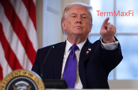 The image features a man dressed in a suit, standing at a podium with his hand extended upwards, pointing towards something off-camera. The man appears to be giving a speech or making an announcement. In the background, there are two American flags, one on each side of the room, which suggests that this event might be taking place in a government building or an official setting.