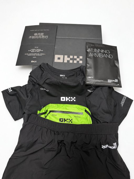 A flat lay of black and neon green OKX athletic apparel including a t-shirt, shorts, running armband, and informational cards with text including 'RUNNING ARMBAND' and 'new money APP'.