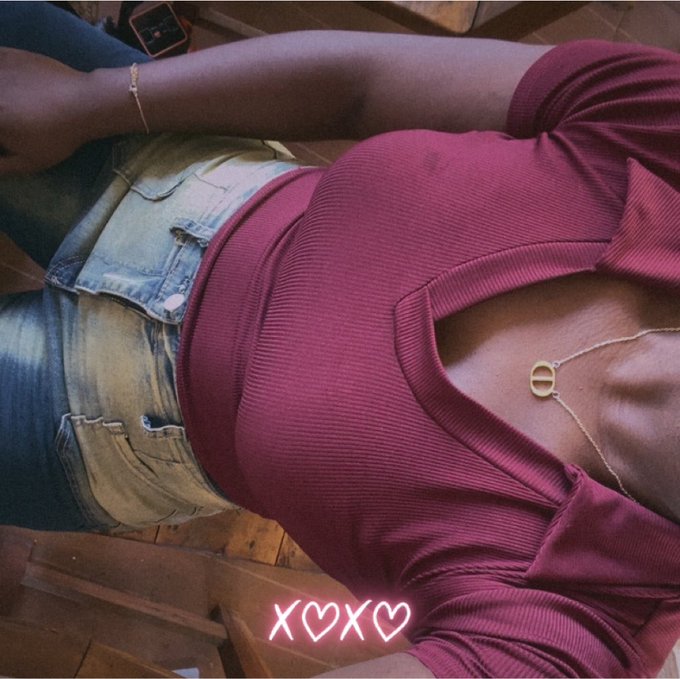 A close-up photo of a person's torso wearing a maroon cutout top and denim shorts, accessorized with a gold necklace, featuring a neon pink 'XOXO' text overlay.